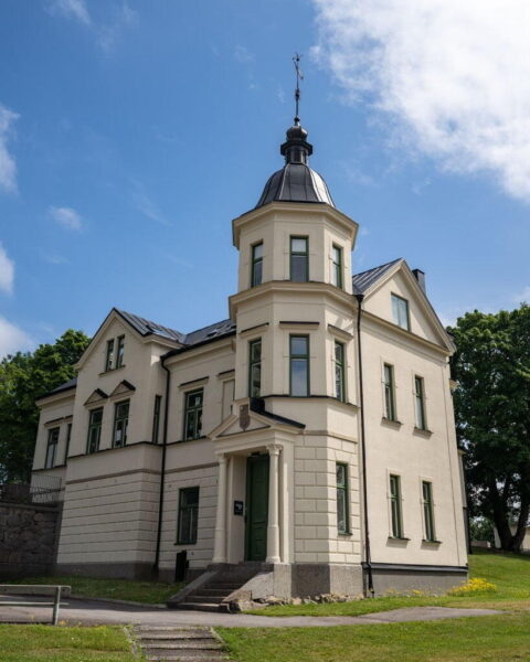 Berga slott i Linköping, elegant herrgårdsbyggnad i ljus puts med oktogonalt torn, grön entré och väderflöjel, omgiven av grönska.