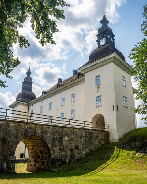 Ekenäs slott i Östergötland med vitputsade väggar, klocktorn och karaktäristiska lökkupoler, omgivet av grön gräsmatta en sommardag