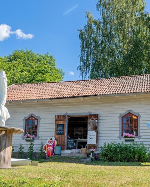 Kinda kanal museum vid Brokind med skylt "Öppet", vitmålat trähus med tegeltak, GB Glace-skylt och blomsterprydda fönster en solig sommardag
