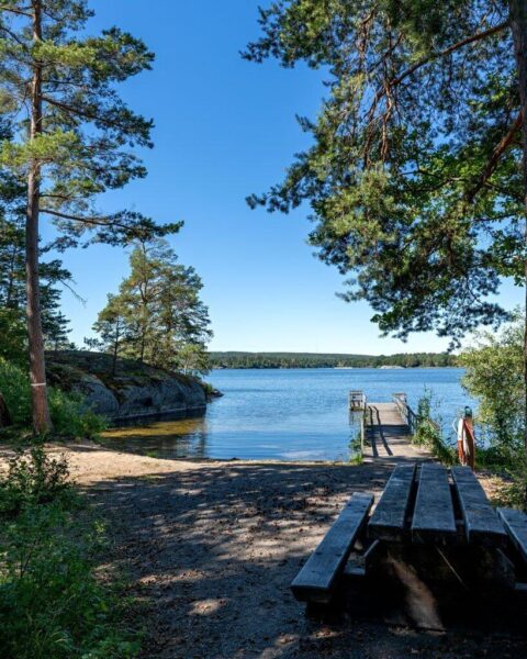 Badplats vid Jaktstugeudden med träbrygga, sittbänk och stilla vatten omgivet av tallar och klippor i Viggeby naturreservat, Östergötland