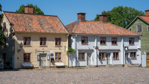 Gamla trähus med tegelpannor vid kullerstenstorg i Gamla Linköping, med gula och vita fasader en solig sommardag