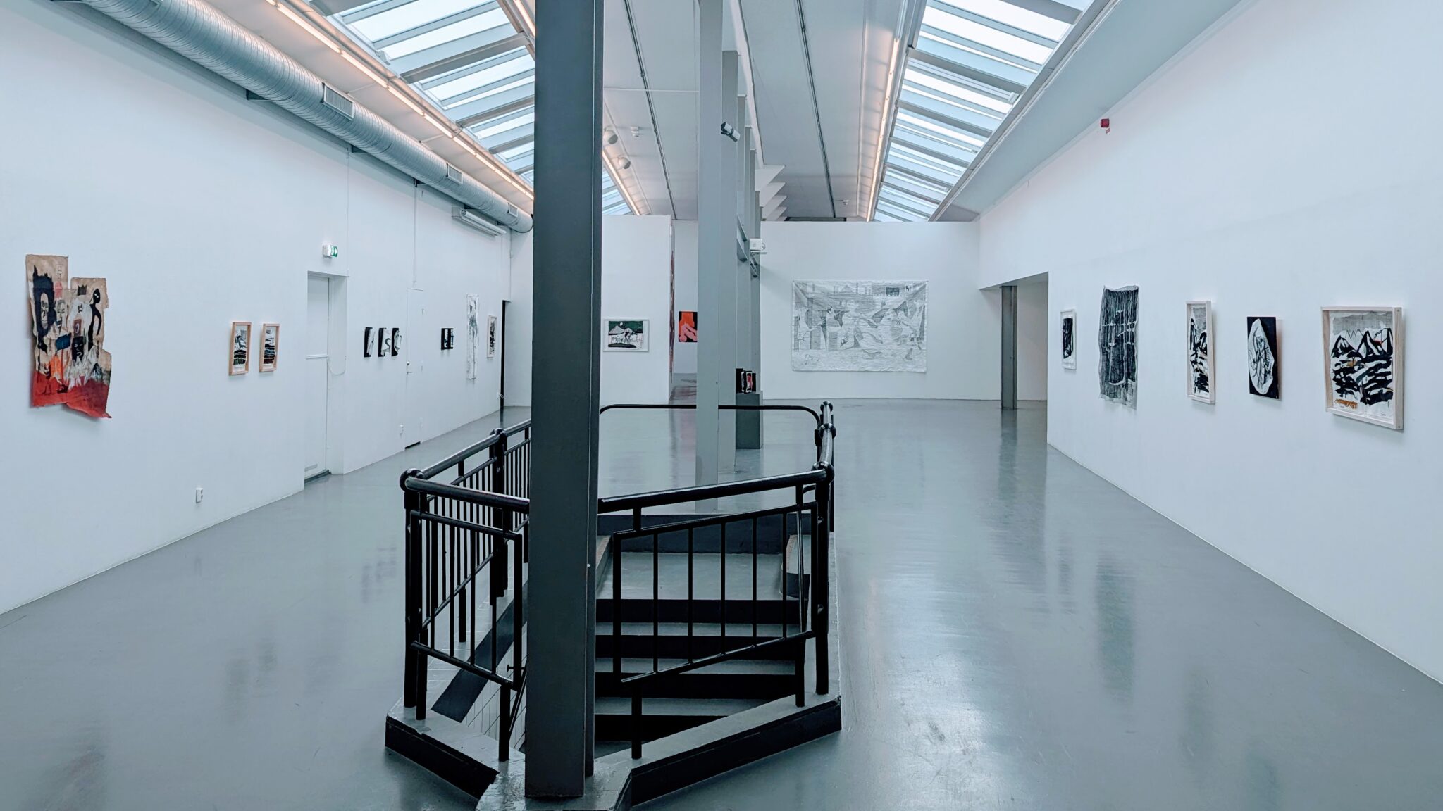 Ljus konsthallssal på Passagen i Linköping med konstverk på vita väggar, svart spiraltrappa och takfönster.