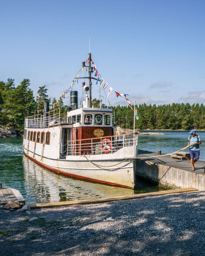 Ellen af Harstena förtöjd vid en brygga i Gryts skärgård, med signalflaggor och tallbevuxna öar i bakgrunden.