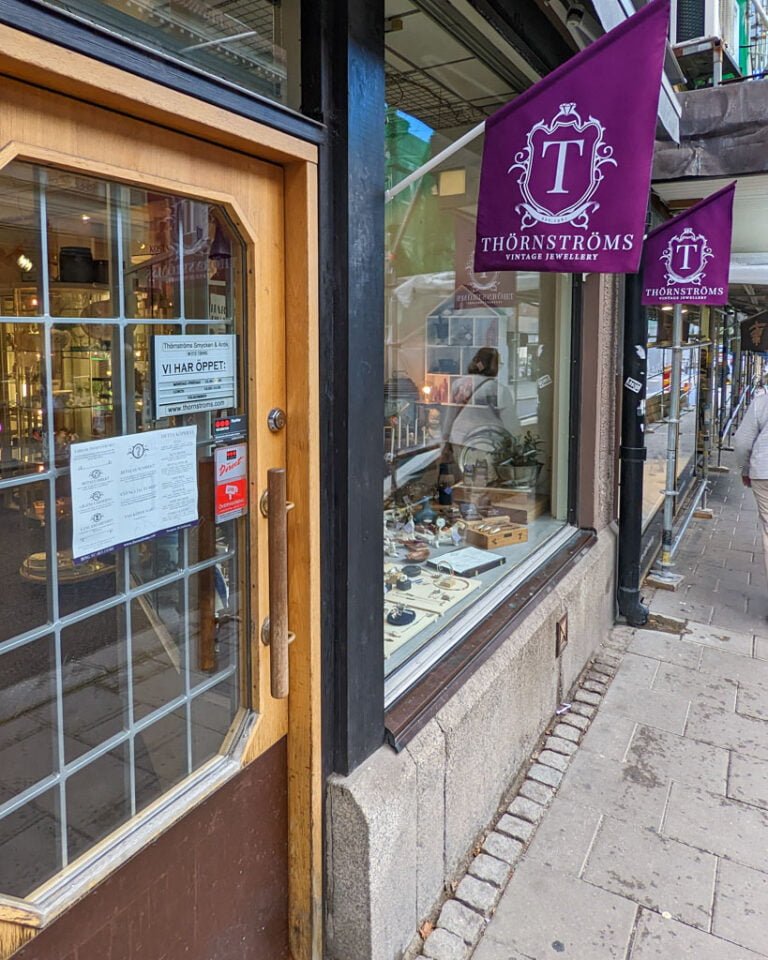 Entrén till Thörnströms Vintage Jewellery i Linköping med skyltfönster fyllt av antika smycken och lila flaggor med butikens logotyp
