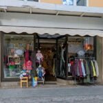 Entrén till Alpha & Omega secondhandbutik i Linköping med skyltfönster fyllda av kläder och en klädställning på trottoaren utanför.