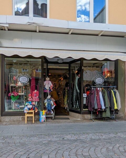 Entrén till Alpha & Omega secondhandbutik i Linköping med skyltfönster fyllda av kläder och en klädställning på trottoaren utanför.