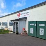 Hjärta till Hjärta Second Hand-butiken i Motala med skylt, entré, insamlingscontainrar och gräsmatta en solig höstdag