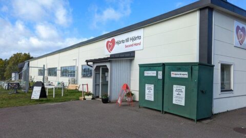 Hjärta till Hjärta Second Hand-butiken i Motala med skylt, entré, insamlingscontainrar och gräsmatta en solig höstdag