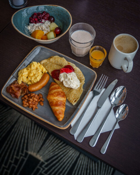 Hotellfrukost på Scandic med croissant, pannkaka, äggröra, korv, bacon, bönor, müsli med frukt, juice och kaffe.