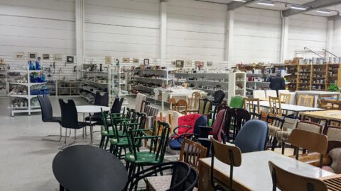 Stor secondhandbutik i Linköping fylld med stolar, bord, porslin och köksutrustning på hyllor längs väggarna.