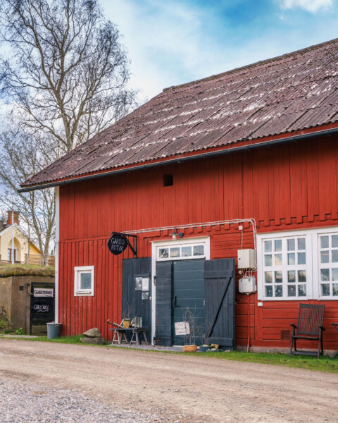 Röd ladugårdsbyggnad med skylt "Gårdsbutik" vid Norrbygård utanför Grebo, med stor mörk port och skyltar till glassterrass och grill