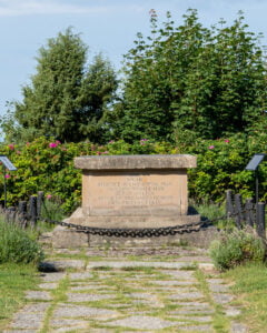 Verner von Heidenstams gravmonument vid Övralid, med inskription omgiven av kedjor, rosenrabatter och grönska.