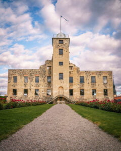 Stjärnorps slottsruin med grusgång, gröna gräsmattor och röda rosor framför den restaurerade 1600-talsfasaden med torn och flagga.