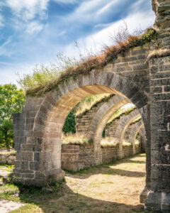 Medeltida stenvalv i rad vid Alvastra klosterruin i Östergötland, med gräs och vegetation som växer på de välbevarade bågar­na.