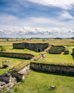 Alvastra klosterruin med gräsbevuxna stenmurar från 1100-talet, omgivet av Östergötlands öppna slättlandskap under sommarblå himmel