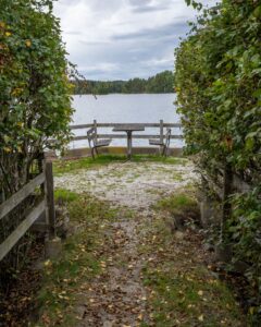 Rastplats med picknickbord vid sjön, inramad av gröna buskar och höstlöv, vid Småängsbadet i Motala kommun.