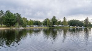 Campingplatser med husvagnar längs strandkanten vid Småängsbadet i Motala, speglande i det stilla vattnet en mulen dag