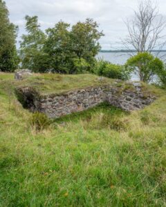 Gräsbevuxna stenmurar från den medeltida borgruinen på Birgittas udde vid sjön Boren, omgivna av grönska och lövträd.