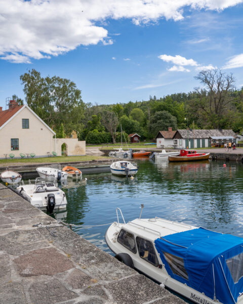 Idyllisk småbåtshamn i Borghamn vid Vättern med förtöjda båtar, stenkajer, äldre byggnader och grön vegetation vid Omberg