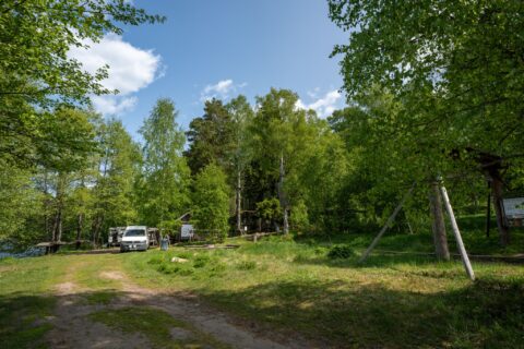 Grön campingplats vid Sörsjöns badplats med husbil parkerad bland lummiga lövträd en solig sommardag i Östergötland