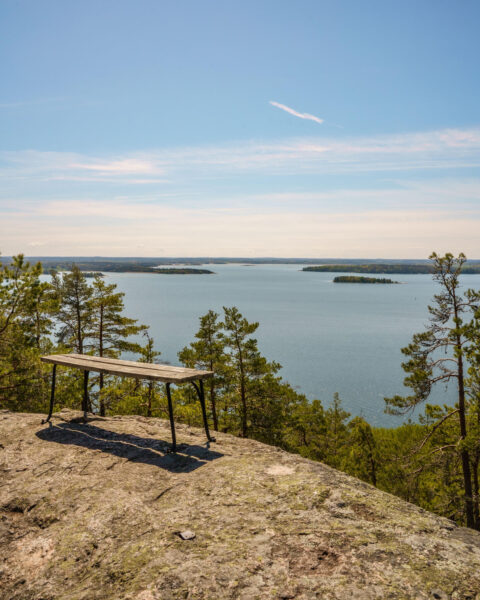 Utsiktsbänk på klipphäll längs Marmorbruksleden i Kolmården med vidstäckt vy över Bråviken och dess öar en solig vårdag