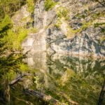 Stilla vatten i Limbergsbrottet längs Marmorbruksleden i Kolmården, med branta marmorklippor som speglas i det gröna vattnet.