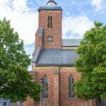 Vårfrukyrkan i Skänninge, medeltida tegelkyrka från 1200-talet med kyrktorn, klocka och gotiska fönster, omgiven av gröna träd.