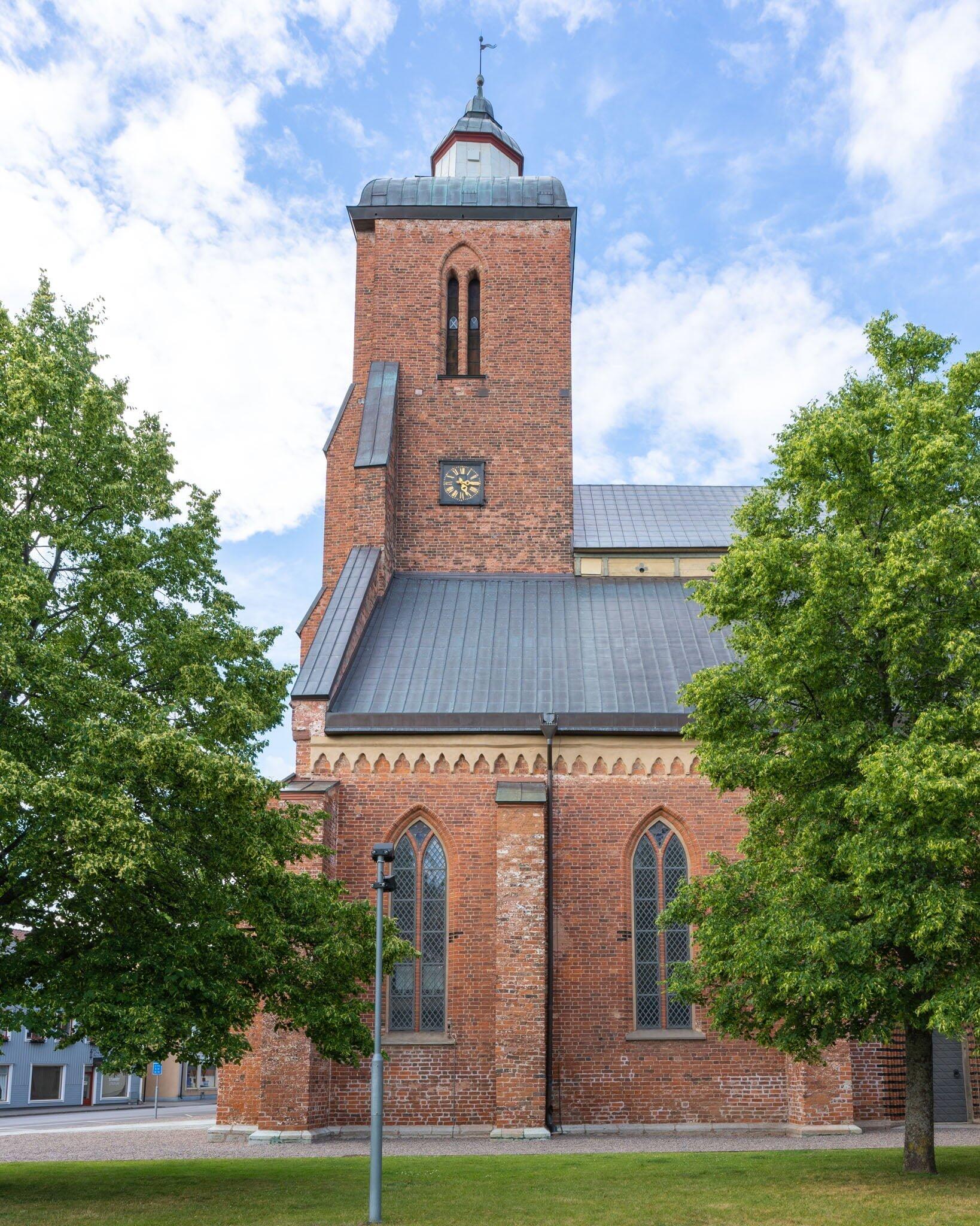Vårfrukyrkan i Skänninge, medeltida tegelkyrka från 1200-talet med kyrktorn, klocka och gotiska fönster, omgiven av gröna träd.