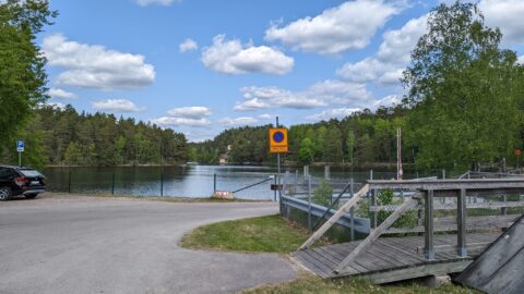 Småbåtshamn vid Åby med brygga, parkering och stilla vatten omgivet av barrskog en solig sommardag i Östergötland