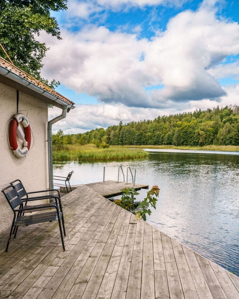 Träbrygga med stolar och livboj vid Glasbruket, med utsikt över stilla vatten omgivet av grön skog nära Göta kanal i Östergötland
