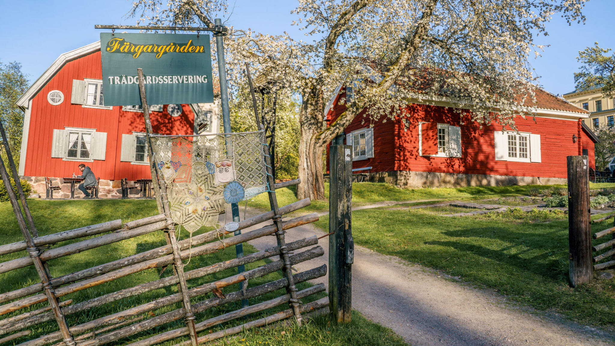 Färgargårdens trädgårdsservering i Norrköping med röda stugor, gärdesgård och blommande träd en solig vårdag
