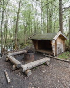 Vindskydd med grillplats och sittbänkar i trä vid vatten i Hallstad Ängar, omgivet av lövskog på våren, Kinda kommun