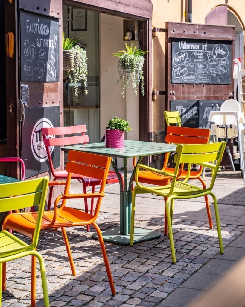 Färgglada stolar i orange, grönt och rosa vid uteserveringen på Tinas Café å Sånt i Knäppingsborg, Norrköping, en solig dag.