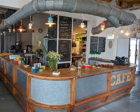 Caféets bardisk i trä och zink med krittavlemenyer, blommor och industriella ventilationsrör på Upperud 9:9 i Dalsland