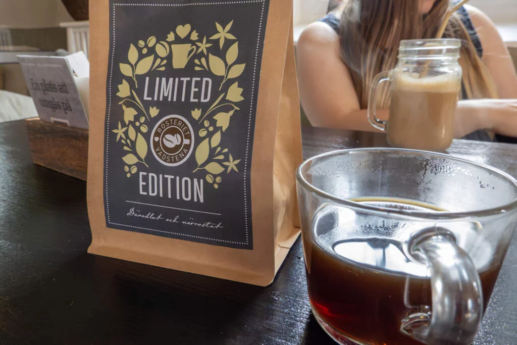Kaffepåse med texten "Limited Edition" från Rosteriet Vadstena bredvid en glasmugg med nybryggt kaffe på cafébordet.