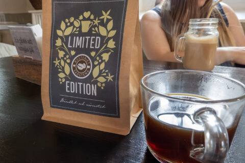 Kaffepåse med texten "Limited Edition" från Rosteriet Vadstena bredvid en glasmugg med nybryggt kaffe på cafébordet.