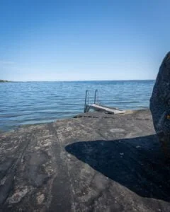 Badstege på slät klipphäll vid Eköns havsbad i Gryt, med stilla skärgårdsvatten och klarblå himmel en solig sommardag.