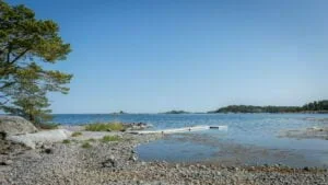 Stenig strand vid Eköns havsbad i Gryts skärgård med badbrygga, tall och utsikt över skärgårdsöar en klarblå sommardag