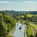 Utsikt från Ramunderberget över Göta kanal med en kanalbåt som glider fram genom grönt sommarlandskap med rapsfält vid Söderköping