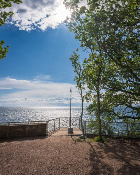 Utsiktsplats vid Stocklycke hamn på Omberg med solglittrande Vättern, dekorativt räcke och grönskande lövträd en sommardag