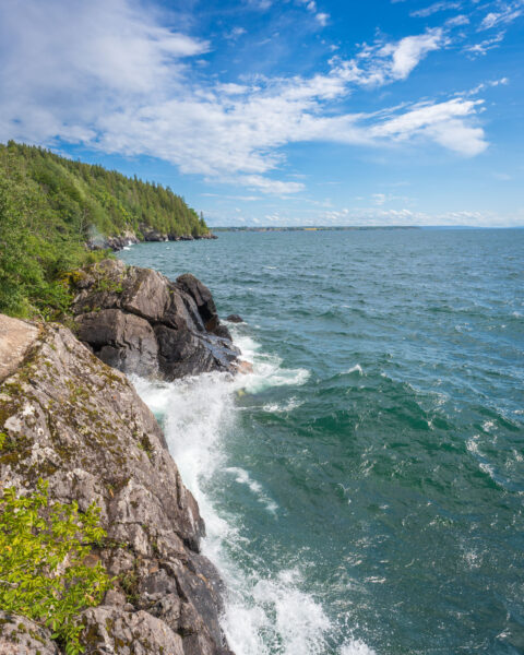 Vågor slår mot klipporna vid Stocklycke hamn på Omberg med utsikt över Vättern och skogsklädd kust en sommardag
