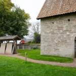 Örberga stenmuseum med medeltida stenhus och uppställda gravhällar under tak på grön kyrkogård, Vadstena kommun