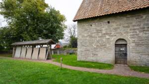 Örberga stenmuseum med medeltida stenhus och uppställda gravhällar under tak på grön kyrkogård, Vadstena kommun