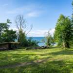 Vindskydd och picknickbord på gröna gräsytan vid Älvarums udde på Omberg med utsikt över Vättern en solig sommardag