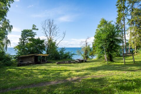 Vindskydd och picknickbord på gröna gräsytan vid Älvarums udde på Omberg med utsikt över Vättern en solig sommardag