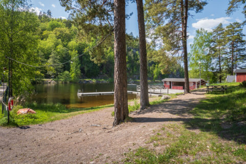 Badplats vid Valö med sandstrand, brygga och röda stugor omgivna av tallar vid sjön Björkern en solig sommardag