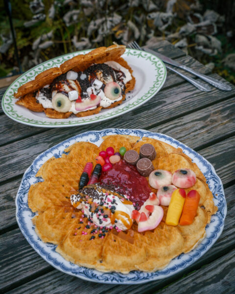 Halloweendekorerade våfflor med sylt, grädde, godis och ögonformade gelégodis på ett utebord vid Skönfärgaregården i Gamla Linköping