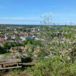 Utsikt över Söderköping från Ramunderberget med en bänk i förgrunden, tak i tegel och grönska en solig vårdag