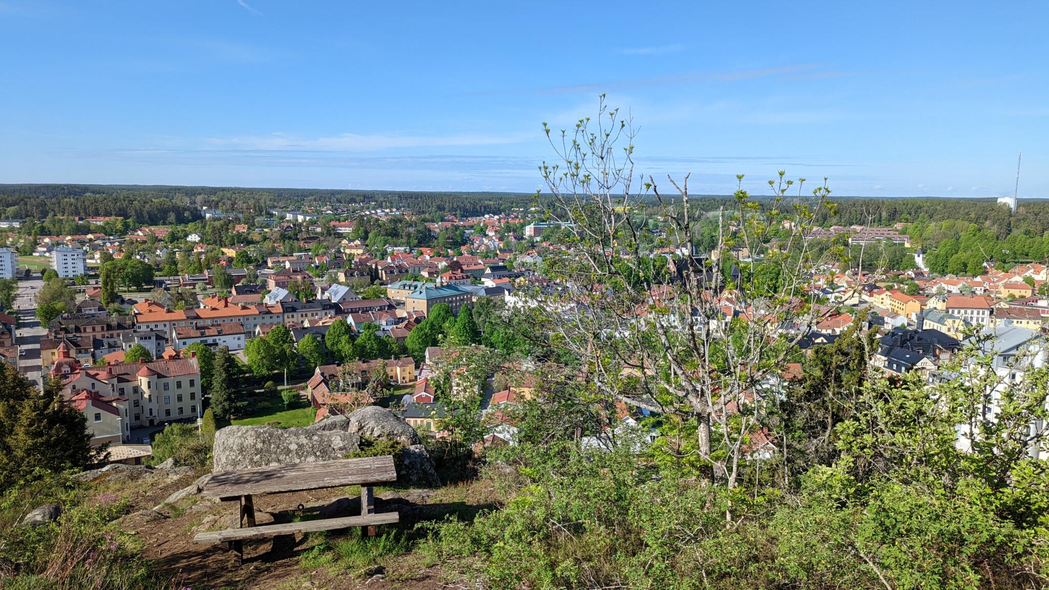 Utsikt över Söderköping från Ramunderberget med en bänk i förgrunden, tak i tegel och grönska en solig vårdag