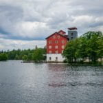 Stora röda silolbyggnaden Upperud 9:9 vid vattnet i Dalsland, omgiven av gröna träd under dramatisk molnhimmel